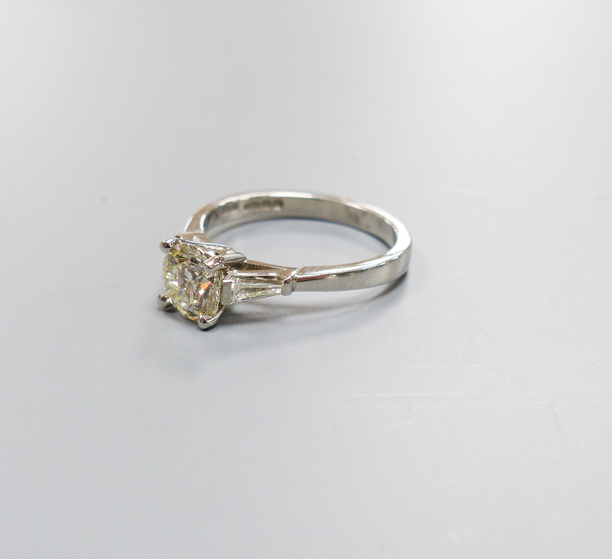 A modern platinum and single stone diamond ring, with trapeze cut diamond set shoulders, size N, gross weight 4.8 grams